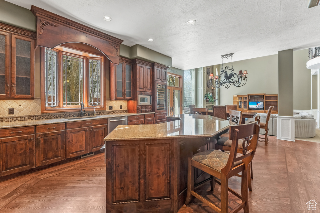 Kitchen with a chandelier, a kitchen island, hardwood / wood-style flooring, white microwave, and a breakfast bar area