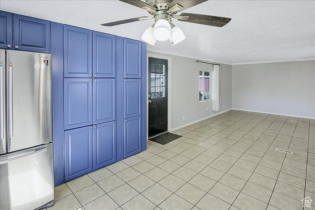 Kitchen featuring ceiling fan, blue cabinets, light tile floors, crown molding, and stainless steel refrigerator