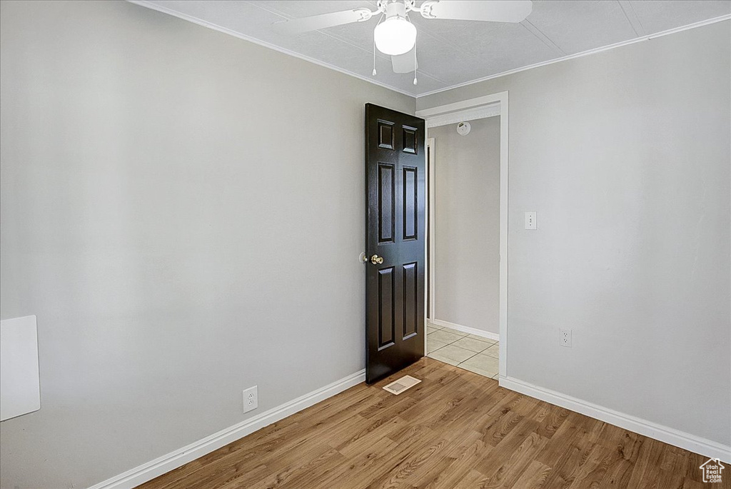 Empty room with ceiling fan, light hardwood / wood-style flooring, and crown molding