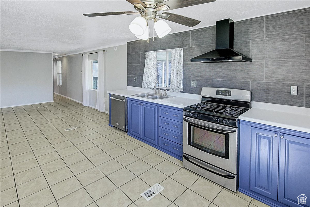 Kitchen with appliances with stainless steel finishes, light tile floors, wall chimney range hood, tile walls, and sink