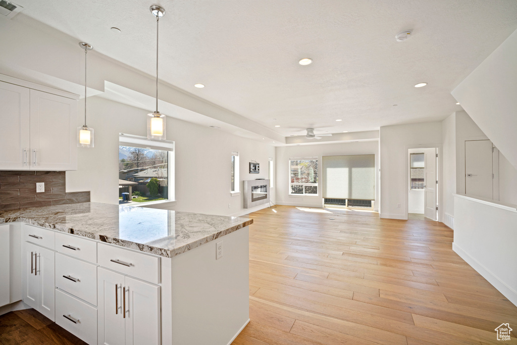 Kitchen with decorative light fixtures, ceiling fan, light hardwood / wood-style floors, white cabinets, and tasteful backsplash