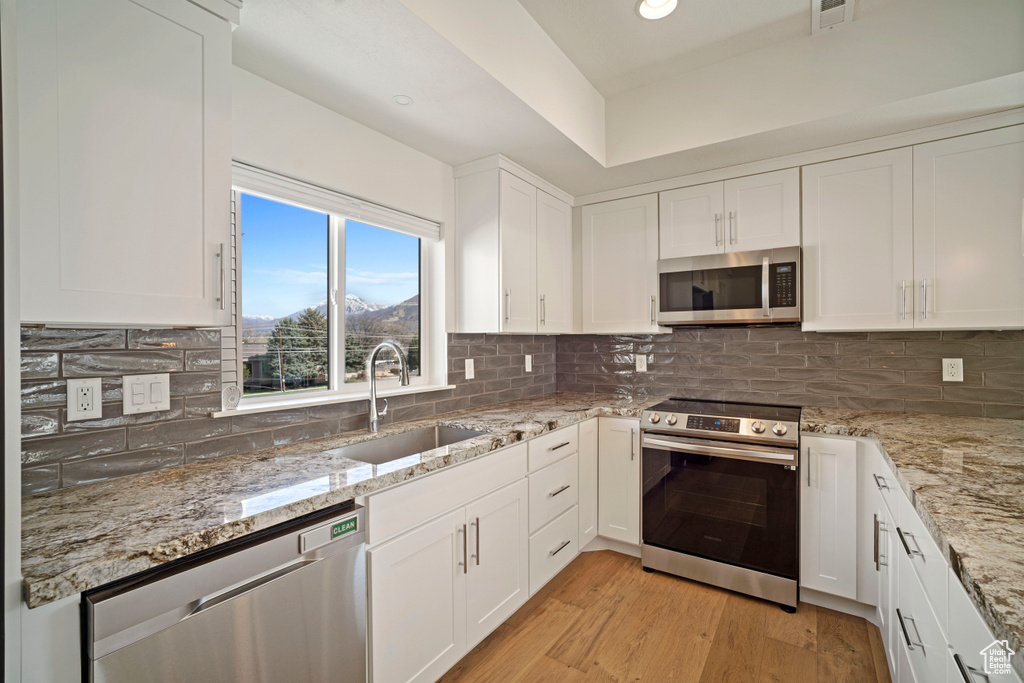 Kitchen with sink, white cabinets, appliances with stainless steel finishes, backsplash, and light hardwood / wood-style floors