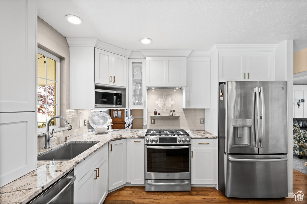 Kitchen featuring sink, hardwood / wood-style floors, white cabinets, appliances with stainless steel finishes, and backsplash