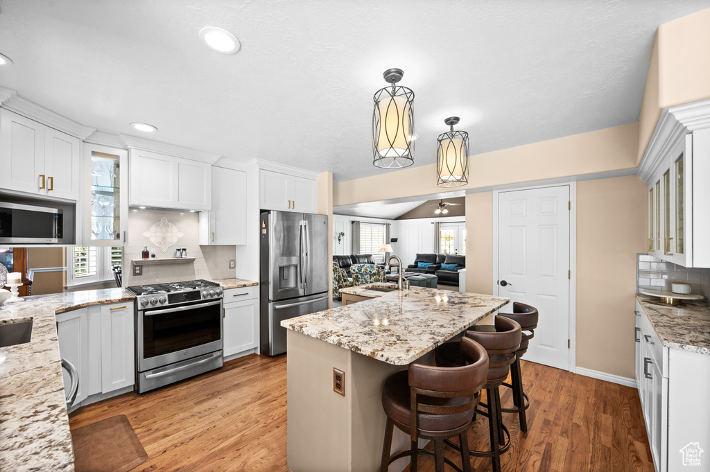 Kitchen featuring hanging light fixtures, a kitchen island with sink, appliances with stainless steel finishes, a breakfast bar area, and hardwood / wood-style flooring