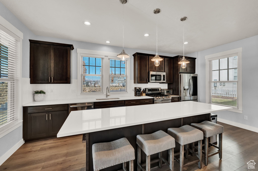 Kitchen featuring a breakfast bar, appliances with stainless steel finishes, decorative light fixtures, and hardwood / wood-style floors