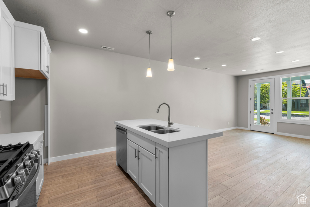 Kitchen with decorative light fixtures, a kitchen island with sink, appliances with stainless steel finishes, light hardwood / wood-style floors, and sink