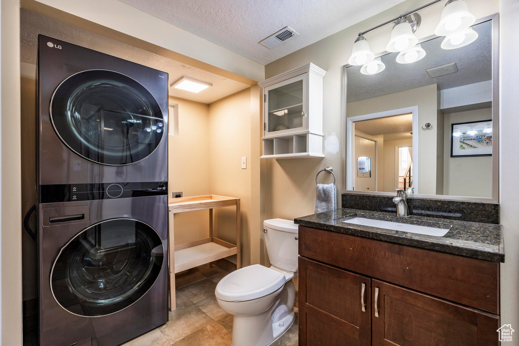Bathroom featuring large vanity, a textured ceiling, tile floors, toilet, and stacked washer / drying machine