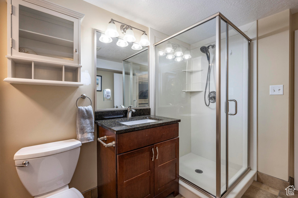 Bathroom with walk in shower, toilet, a textured ceiling, vanity, and tile floors