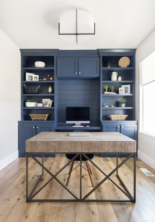 Home office featuring built in shelves and light hardwood / wood-style flooring