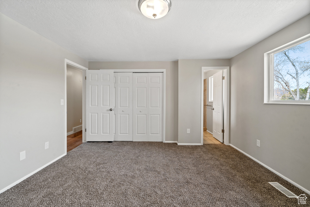 Unfurnished bedroom with light carpet, ensuite bath, a closet, and a textured ceiling
