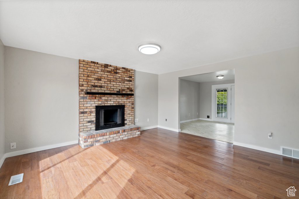 Unfurnished living room with brick wall, hardwood / wood-style floors, and a brick fireplace