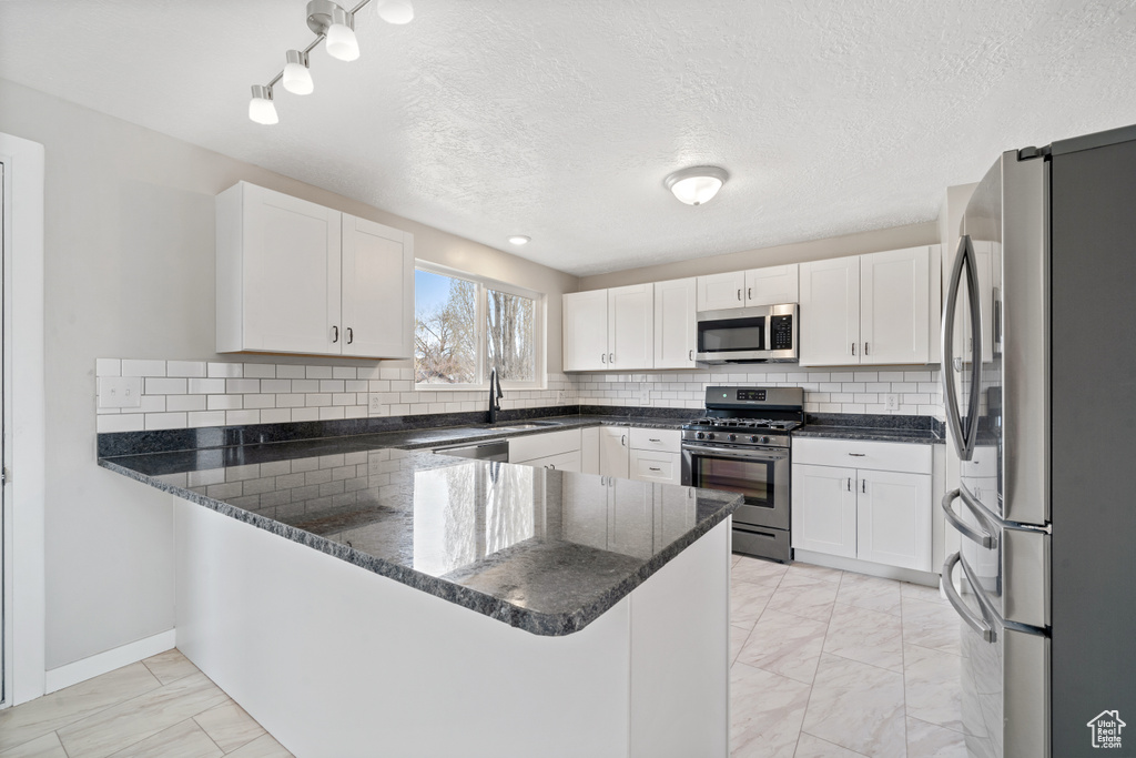 Kitchen featuring tasteful backsplash, stainless steel appliances, dark stone countertops, light tile floors, and kitchen peninsula