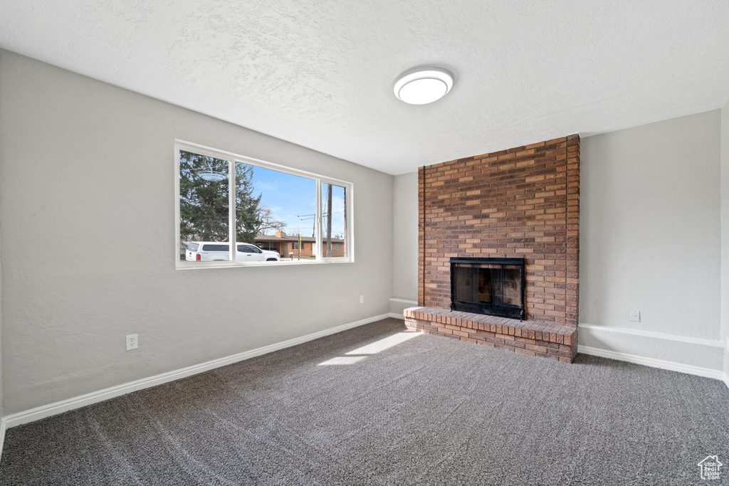 Unfurnished living room featuring a textured ceiling, dark carpet, brick wall, and a brick fireplace