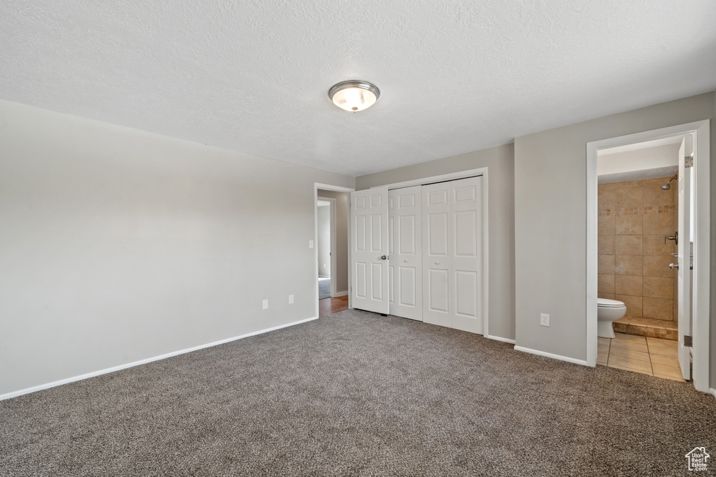 Unfurnished bedroom with light colored carpet, ensuite bathroom, and a textured ceiling