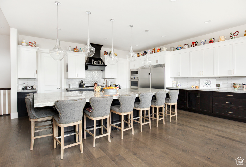 Kitchen featuring backsplash, an island with sink, white cabinets, dark hardwood / wood-style flooring, and built in appliances