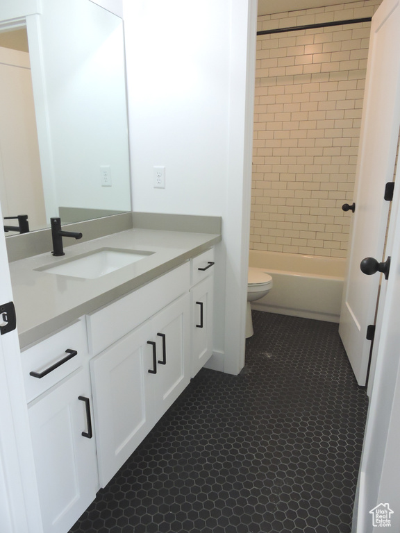 Full bathroom featuring toilet, tile floors, vanity, and tiled shower / bath