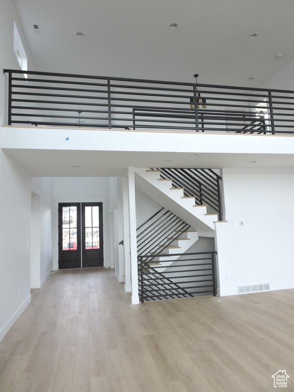 Stairs featuring french doors, light wood-type flooring, and a high ceiling