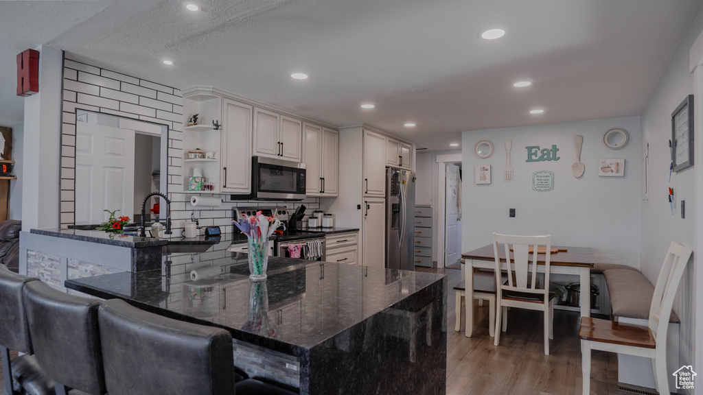 Kitchen with stainless steel appliances, dark stone counters, kitchen peninsula, light hardwood / wood-style flooring, and backsplash