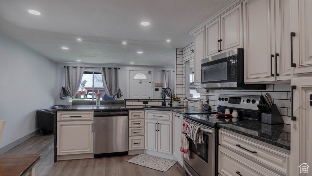 Kitchen with kitchen peninsula, dark stone countertops, backsplash, stainless steel appliances, and light wood-type flooring