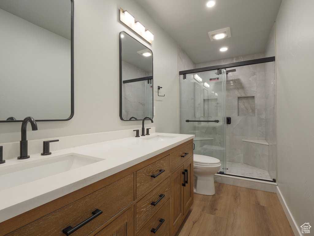 Bathroom featuring an enclosed shower, double sink, toilet, oversized vanity, and hardwood / wood-style flooring