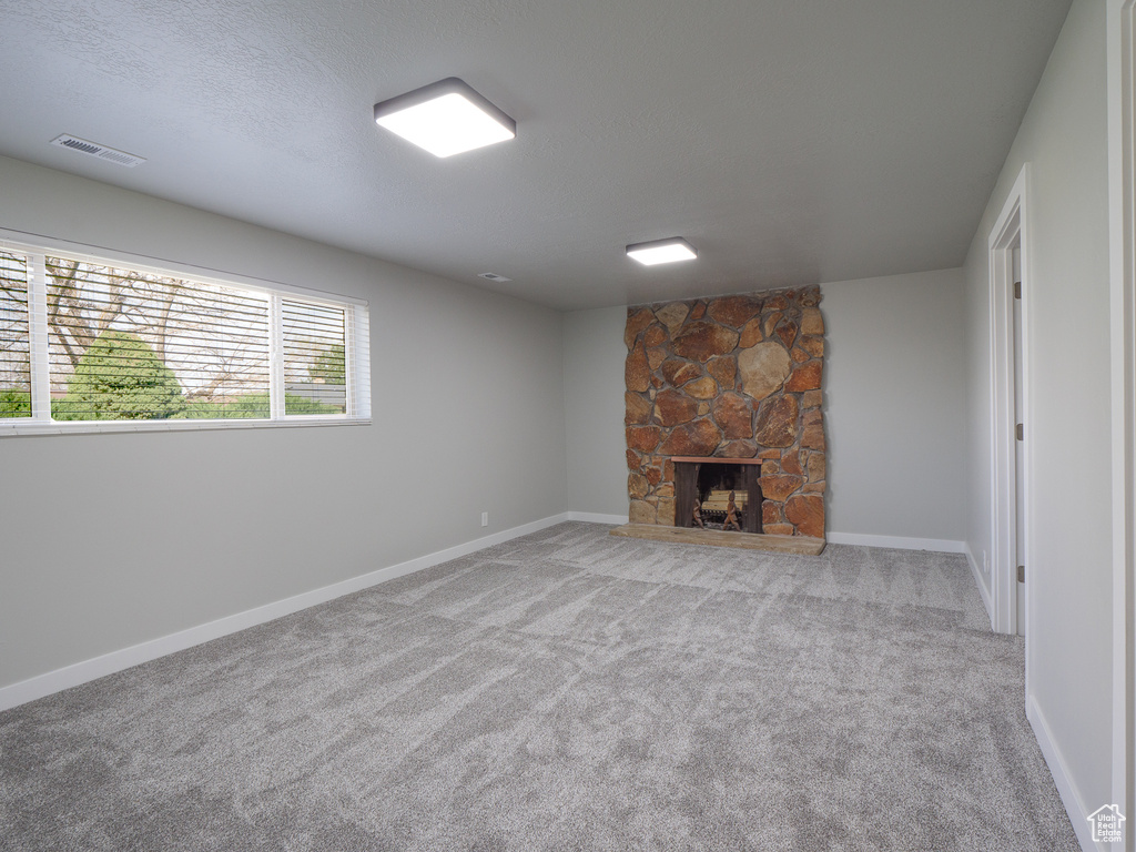 Unfurnished living room featuring a wealth of natural light, a stone fireplace, and light colored carpet