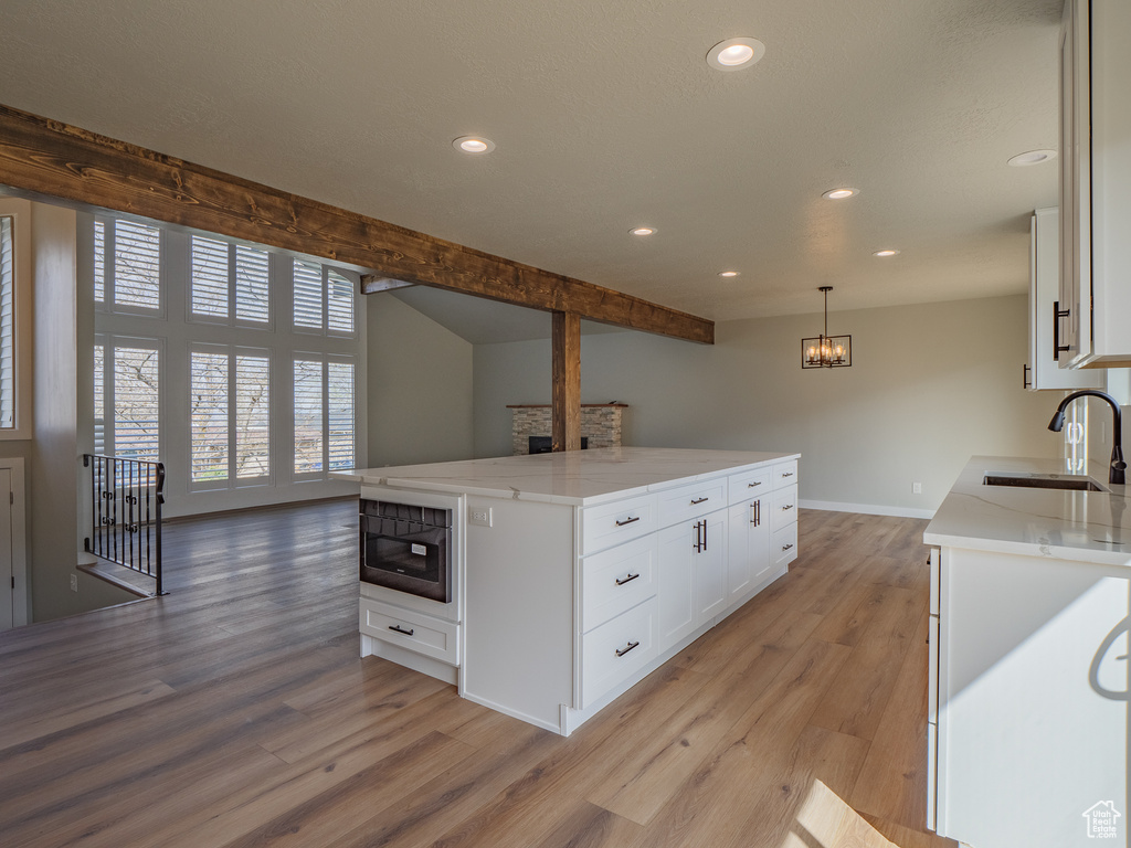 Kitchen featuring sink, hanging light fixtures, white cabinets, light hardwood / wood-style flooring, and a notable chandelier