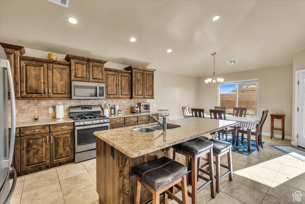 Kitchen with a breakfast bar, appliances with stainless steel finishes, light tile floors, a notable chandelier, and sink