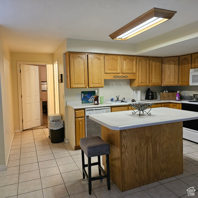 Kitchen with light tile floors, a center island, white appliances, a breakfast bar area, and sink