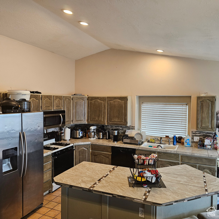 Kitchen featuring backsplash, light tile flooring, sink, stainless steel appliances, and vaulted ceiling