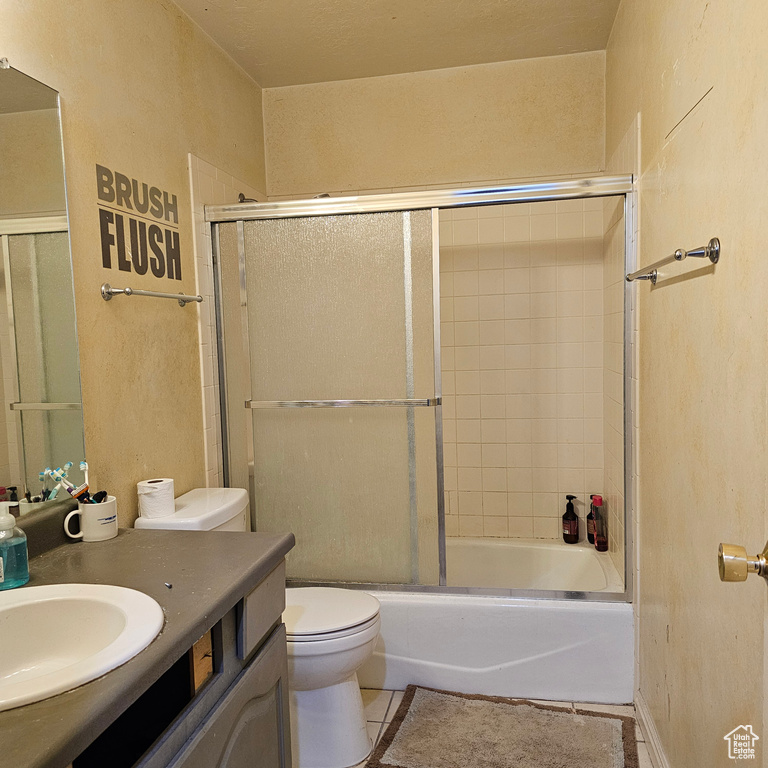 Full bathroom with tile floors, shower / bath combination with glass door, toilet, and vanity