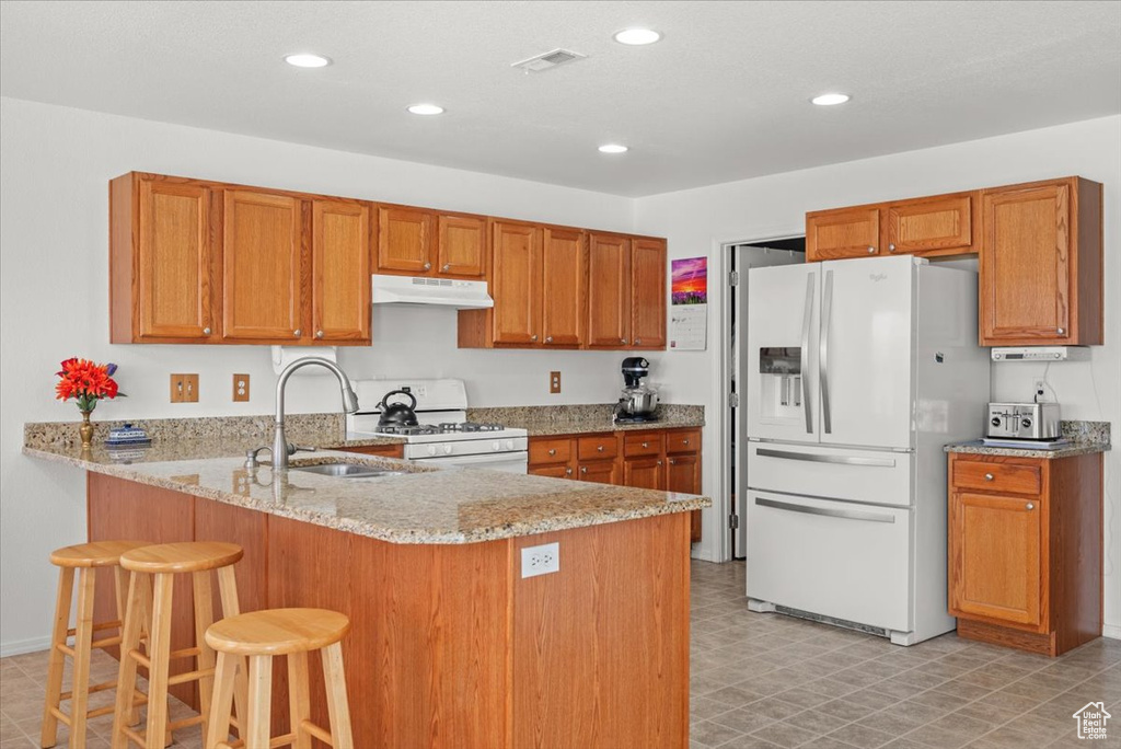 Kitchen with light tile flooring, light stone counters, a breakfast bar, white appliances, and sink