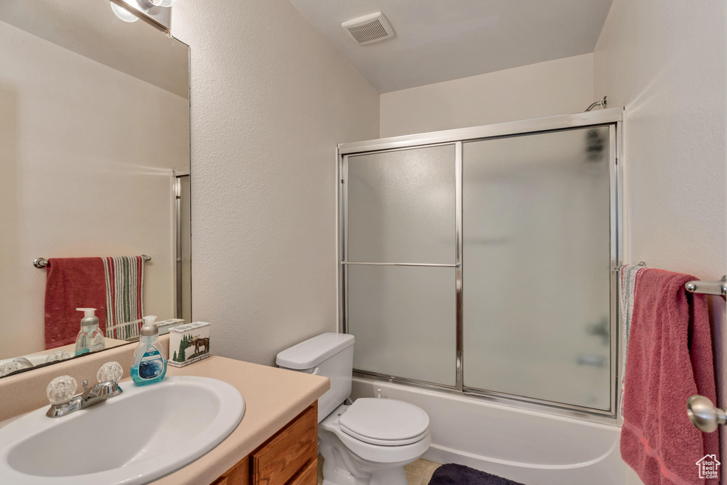 Full bathroom with tile flooring, combined bath / shower with glass door, toilet, and large vanity