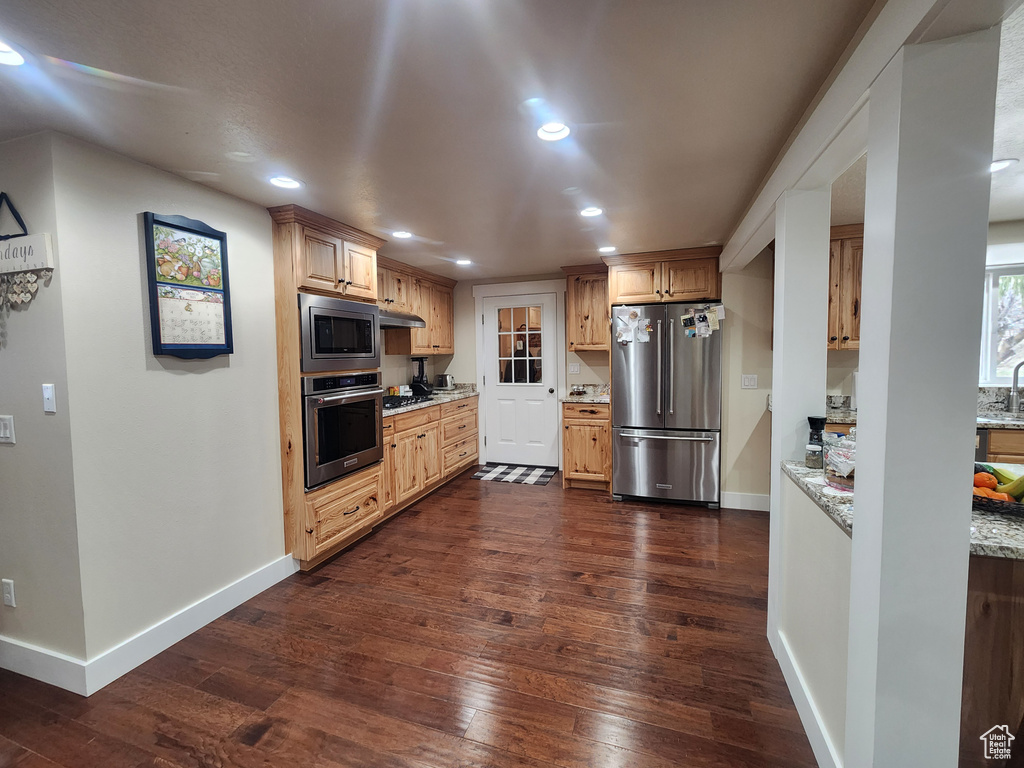 Kitchen with light stone counters, appliances with stainless steel finishes, and dark hardwood / wood-style floors
