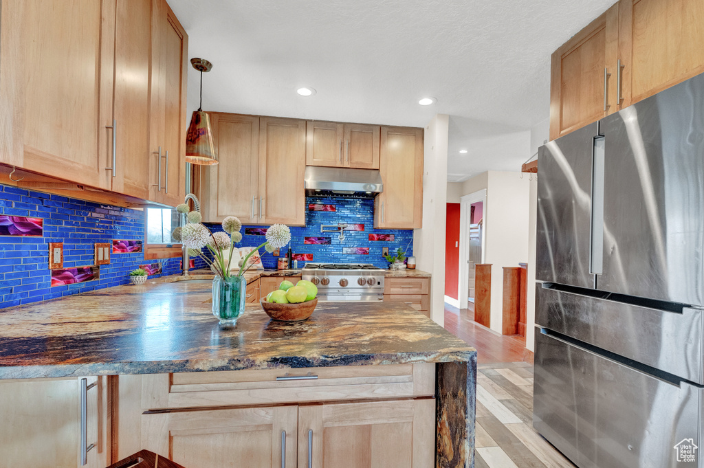Kitchen featuring light hardwood / wood-style floors, dark stone countertops, stainless steel appliances, backsplash, and wall chimney range hood