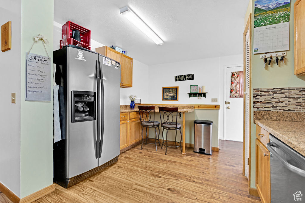 Kitchen with appliances with stainless steel finishes, backsplash, light wood-type flooring, and a breakfast bar