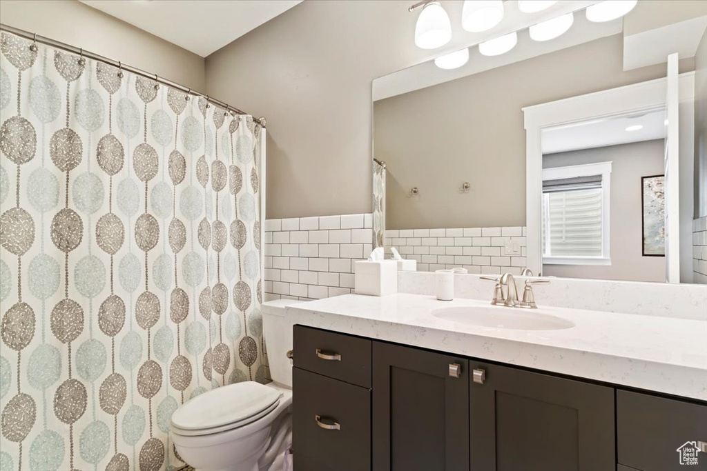 Bathroom with toilet, vanity with extensive cabinet space, tasteful backsplash, and tile walls