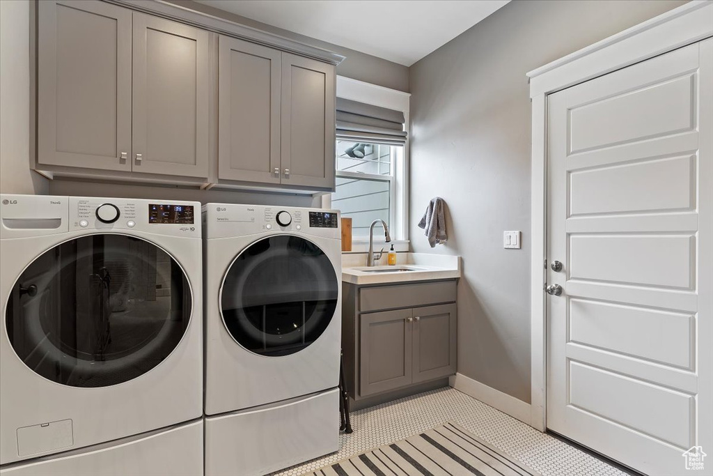 Washroom with light tile flooring, washer and clothes dryer, cabinets, and sink