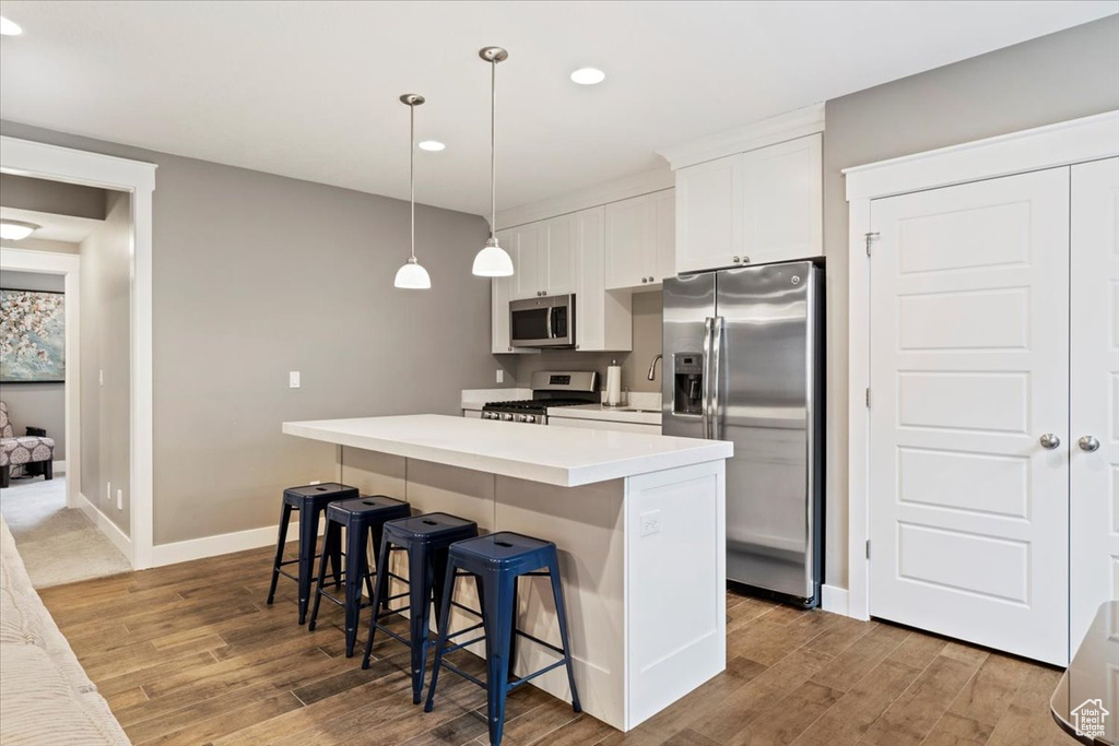 Kitchen with a kitchen island, stainless steel appliances, white cabinetry, and wood-type flooring