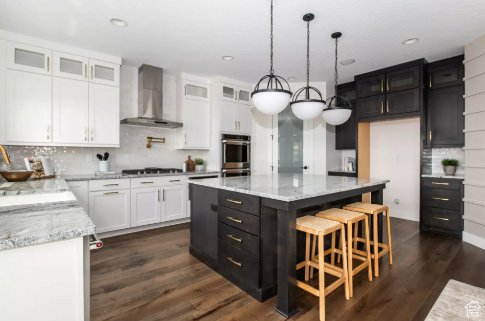 Kitchen with a kitchen island, wall chimney range hood, backsplash, light stone counters, and dark hardwood / wood-style flooring