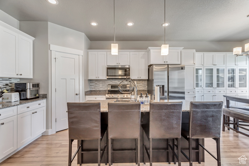 Kitchen with hanging light fixtures, stainless steel appliances, light wood-type flooring, and tasteful backsplash