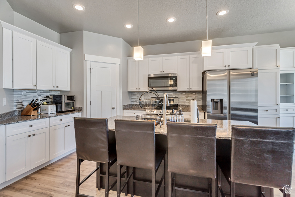Kitchen featuring white cabinets, pendant lighting, backsplash, and stainless steel appliances