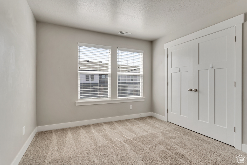 Unfurnished bedroom with a closet, a textured ceiling, and light colored carpet