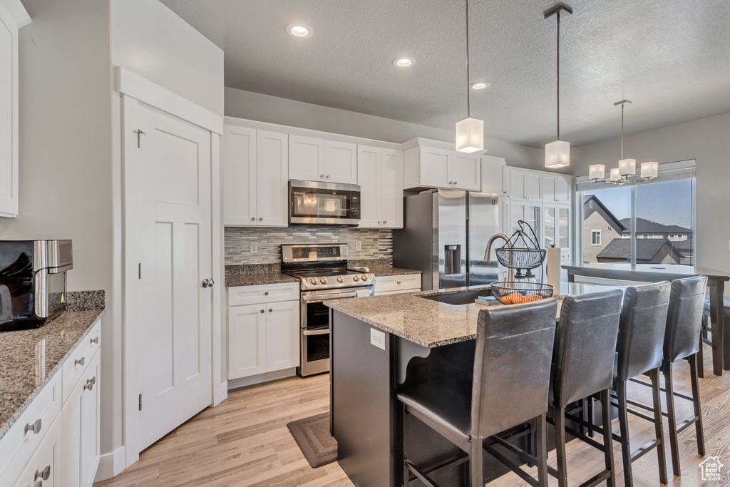 Kitchen featuring a chandelier, stainless steel appliances, decorative light fixtures, light hardwood / wood-style flooring, and light stone counters
