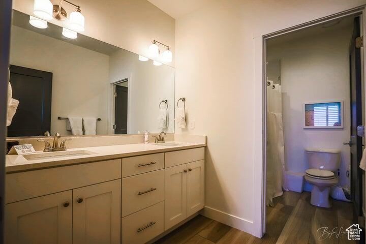 Bathroom featuring hardwood / wood-style flooring, toilet, and dual bowl vanity