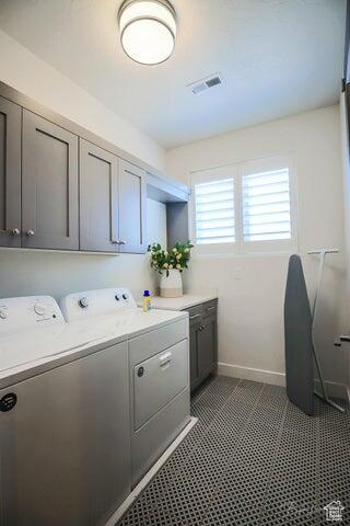 Laundry room featuring washing machine and dryer, cabinets, and dark tile flooring