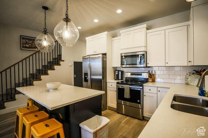 Kitchen with appliances with stainless steel finishes, backsplash, wood-type flooring, decorative light fixtures, and white cabinetry