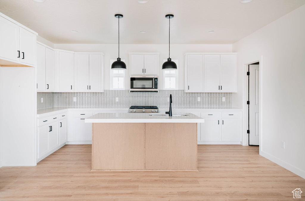 Kitchen featuring white cabinetry, an island with sink, tasteful backsplash, and light wood-type flooring