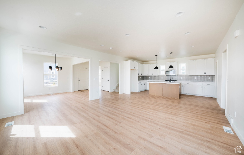 Kitchen with white cabinets, pendant lighting, light hardwood / wood-style floors, and a kitchen island with sink
