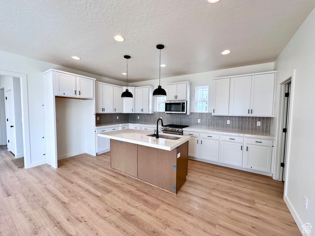 Kitchen with decorative light fixtures, light hardwood / wood-style floors, a kitchen island with sink, and white cabinets