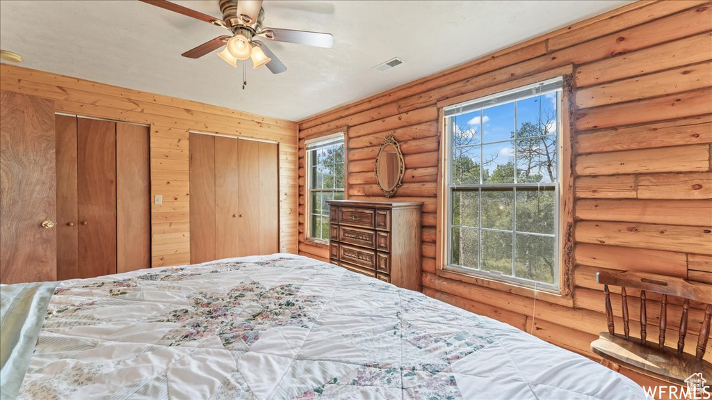 Bedroom with multiple closets, ceiling fan, and rustic walls